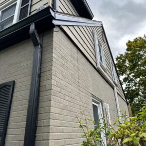 A ground level view of a completed gutter project on a residential home with brick and vinyl siding.