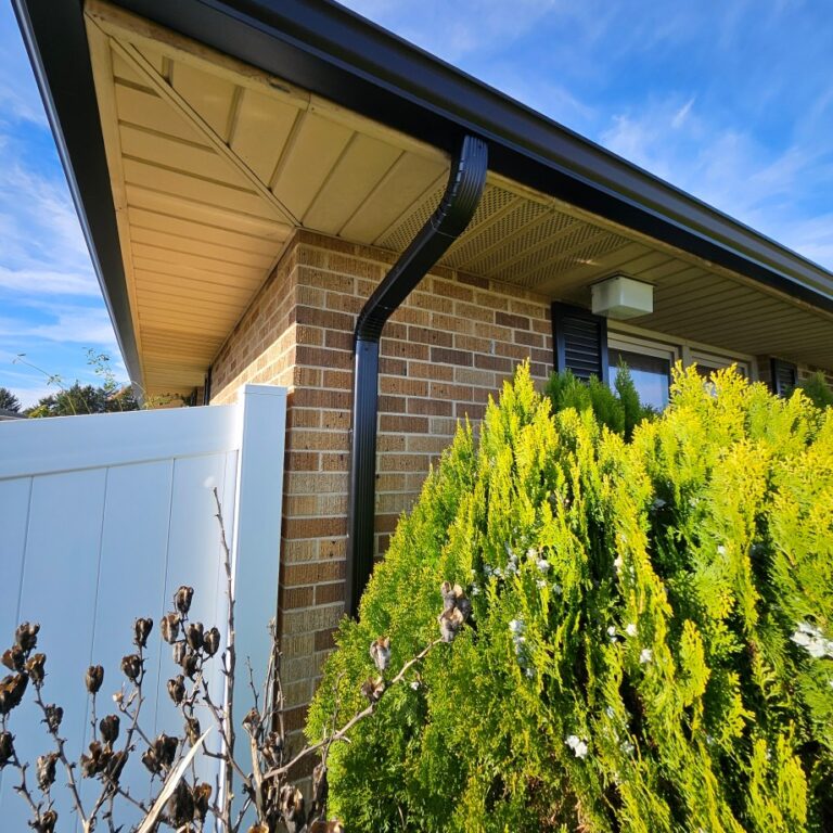 Upward view of a new installed black gutter on a residential home that has a roof overlapping the home.