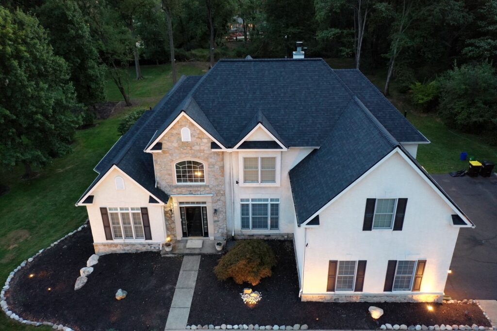Aerial view of a large two-story home featuring a newly installed dark shingle roof, showcasing professional roof replacement and enhanced curb appeal on a residential property surrounded by trees.