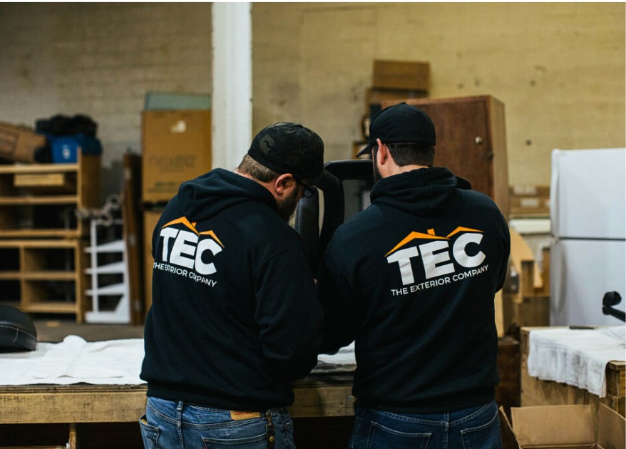 Two TEC employees wearing company hoodies, facing away from the camera, working together on something.