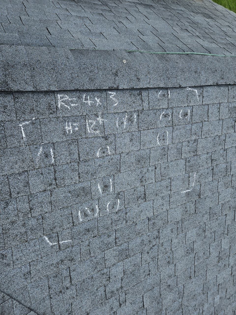 Inspector chalk-marking hail hits on asphalt shingles for insurance documentation